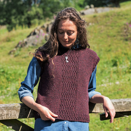 A woman wears a handknit sweater vest over a shirt. the vest has a textured stitch pattern over the centre front.