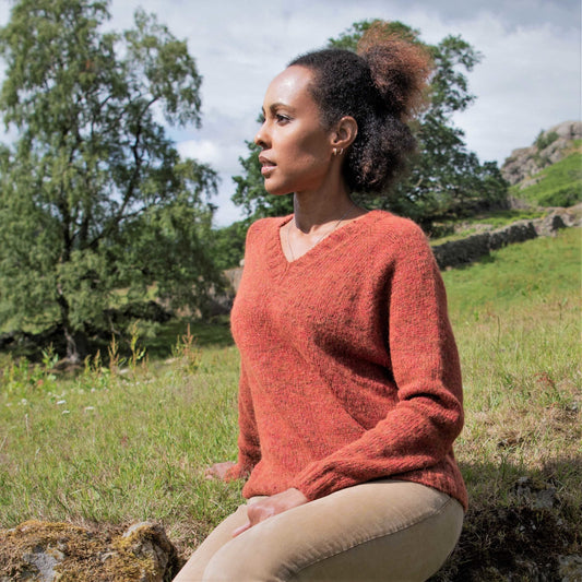 Women sat in a valley, wearing an burt orange knitter sweater